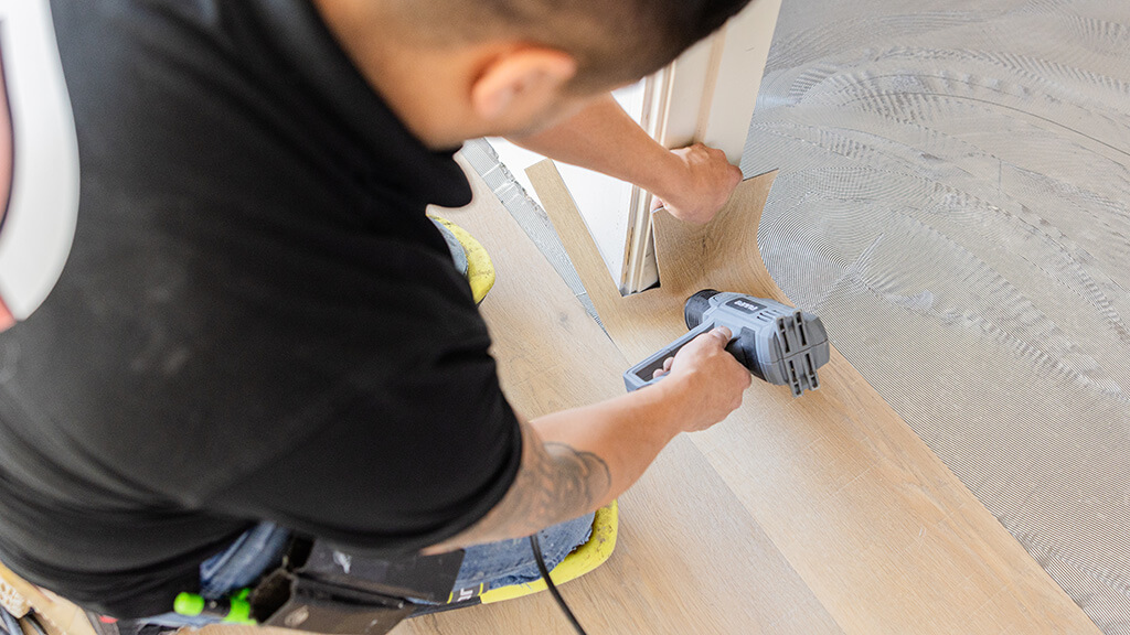 Vloerenspecialist lijmt pvc tegels met houtlook op ondervloer